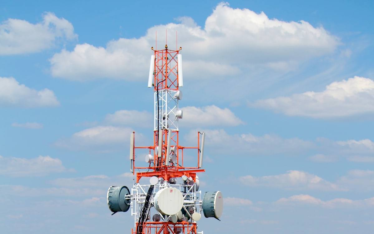 Topo de torre de telecomunicações com antenas setoriais e enlaces de micro-ondas
