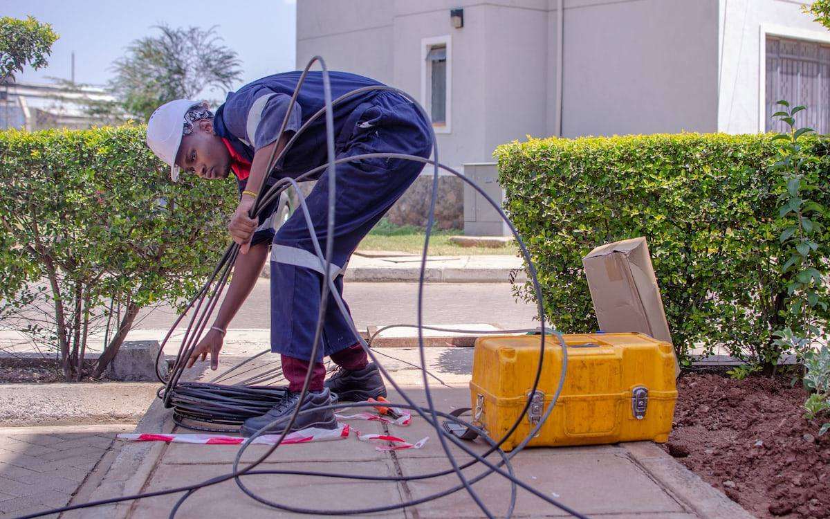 Técnico puxando lance de cabo óptico em caixa de passagem na calçada de uma residência