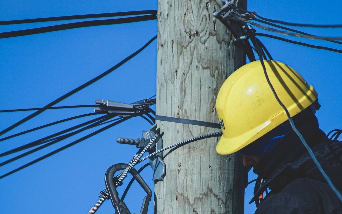 Técnico de capacete trabalhando em cabos ópticos aéreos presos a um poste